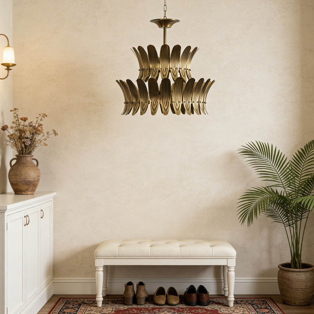 Vintage brass leaf chandelier hanging in a neutral-toned entryway with a bench and potted plants.