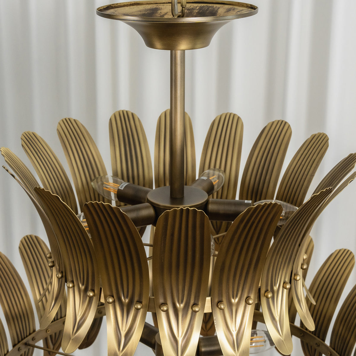 Vintage brass leaf chandelier turned on, showing its warm ambient light and layered design.