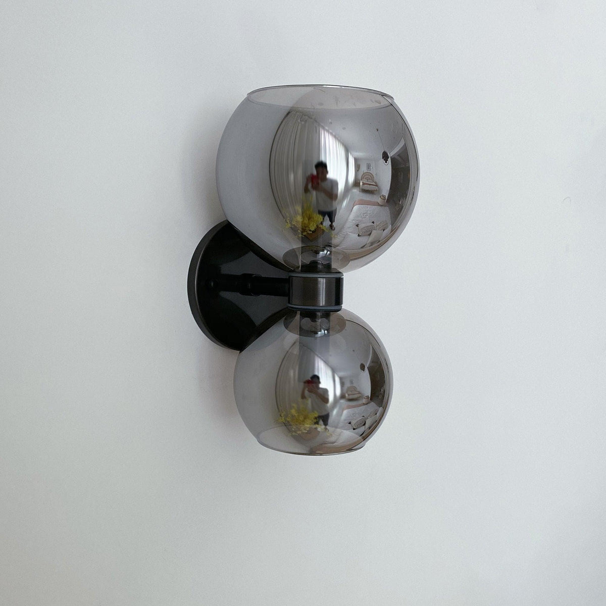 Modern wall sconce with dual smoked glass globes and black metal mount, reflecting room interior.