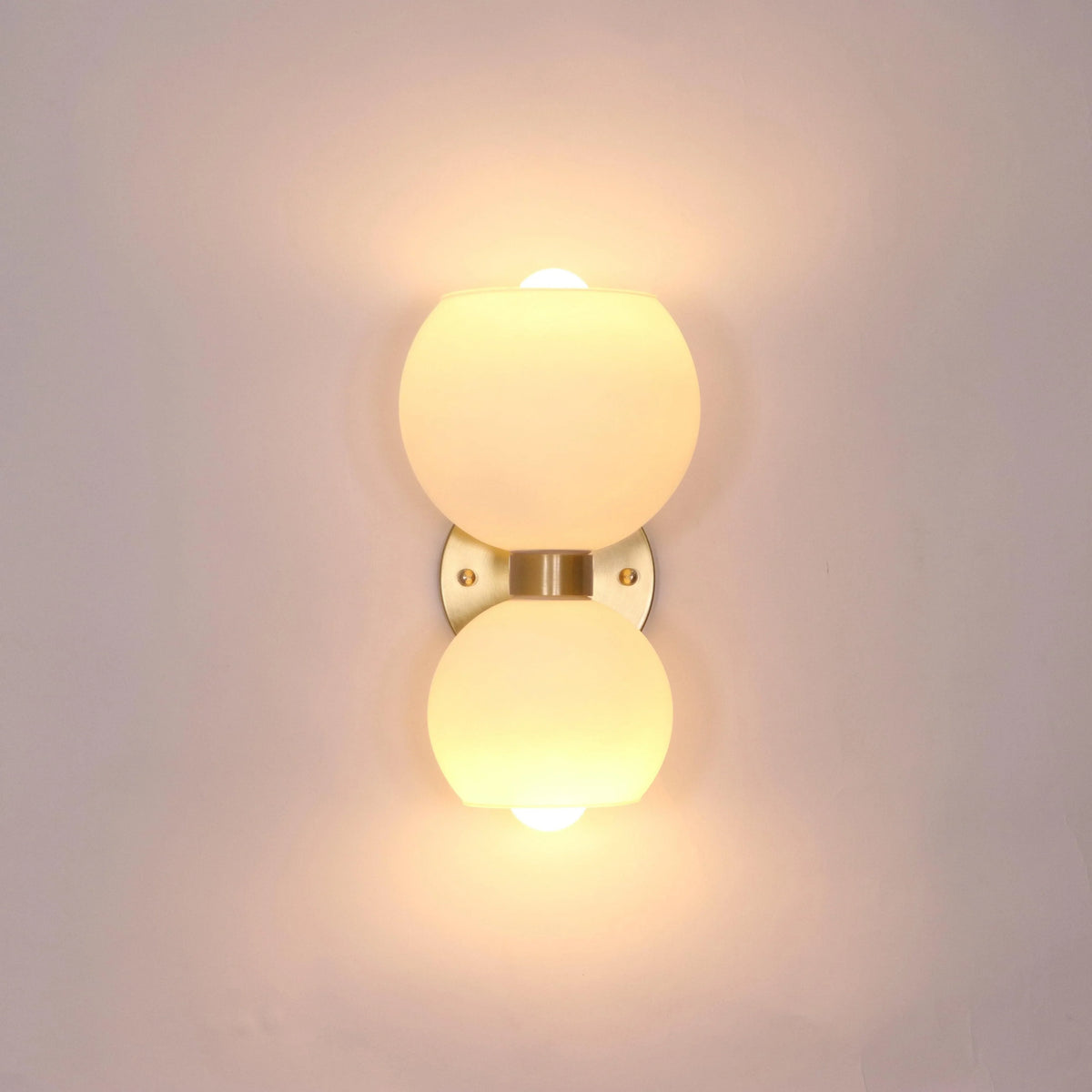 Modern wall sconce with frosted glass globes and brass finish, emitting warm ambient light.
