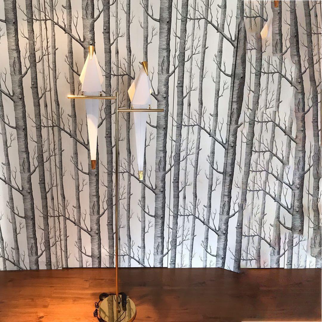 Modern floor lamp with geometric white shades and gold accents against forest wallpaper